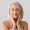 Mature woman giving herself face massage on light background